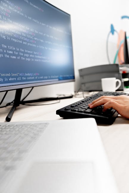A close-up photograph of a computer screen displaying lines of HTML code in various colors, including blue, green, red, and yellow, set against a dark background. The code includes tags for headings, 